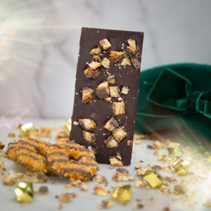 A bar of Appalachian Standard's Caramel Bliss Cookie THC Chocolate with cookies in the front and a green hat in the back