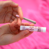 Hands holding Appalachian Standard's 'Rollin' in the Sheets' pre-roll package and a joint against a bright pink background. The pink packaging features rose designs and indicates it contains a 1:1 CBD and THC blend.